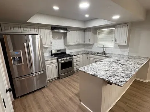 The same kitchen after renovation, with white cabinets, granite counters and new wood-look flooring.